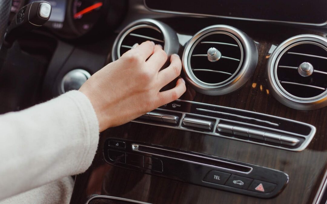 Person adjusting the air system to cool off on a black plastic control panel in a car